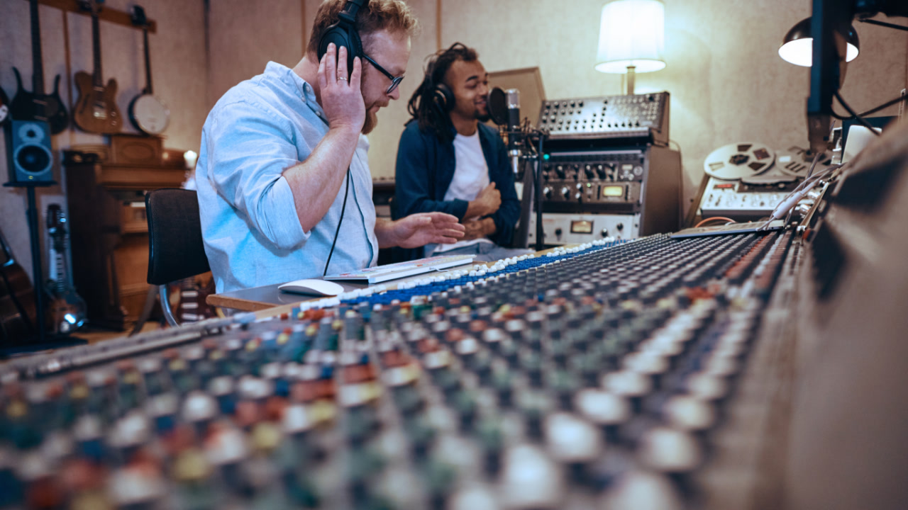 Music producer works at soundboard while listening to a singer in a recording studio